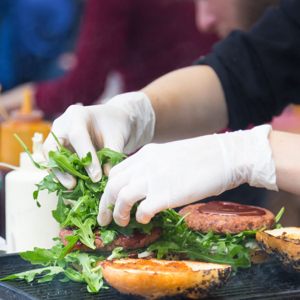 Ein chef legt frischen rucola mit hygonorm safe fit nitril-handschuhen weiß behandschuht auf einen gegrillten burgerpatty