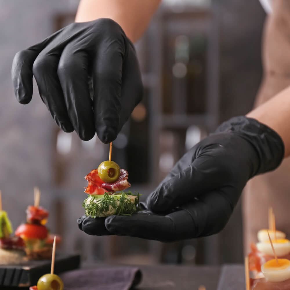 Ein handcrafted appetizer skewer mit grüner olive, rotem cured meat, dill und gurke, präsentiert mit hygostar safe light nitril-handschuhe schwarz 100 stück