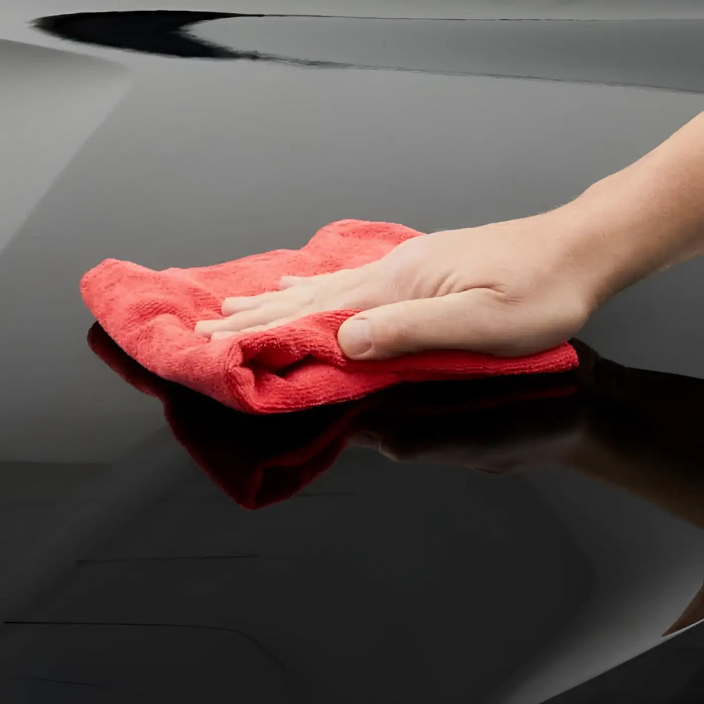 Ein rotes mikrofasertuch wischt eine glänzende schwarze oberfläche mit sonax autopolitur mit carnauba