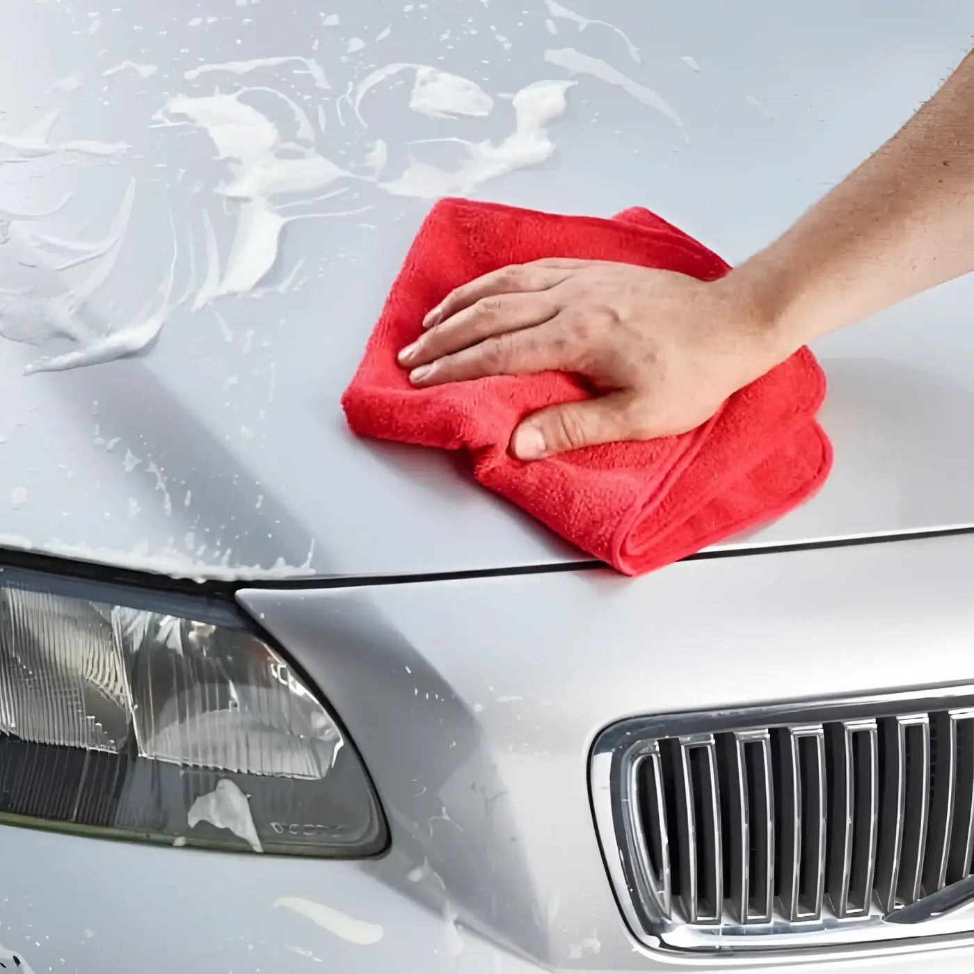 Ein lebendiges rotes mikrofasertuch wird verwendet, um die motorhaube eines silbernen autos mit sonax clay-ball kratzfrei zu reinigen