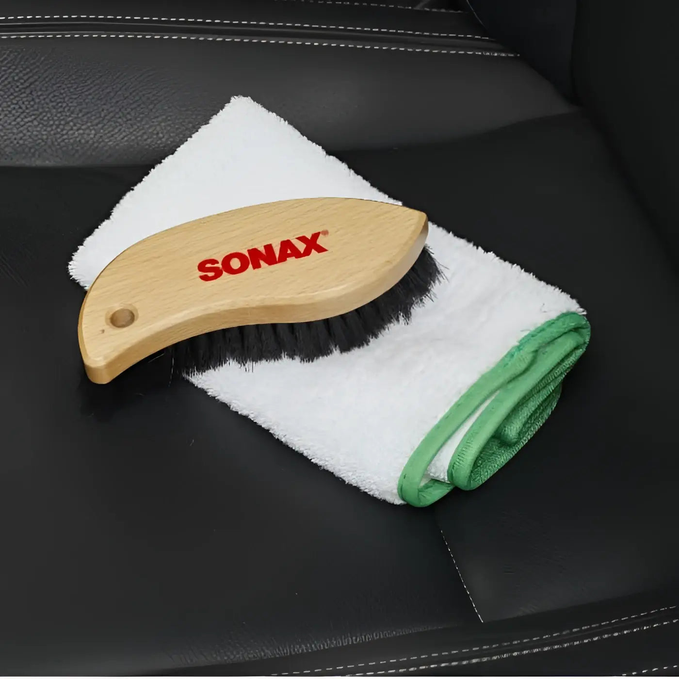 Sonax textil und lederbürste mit hellem griff aus holz und schwarzen borsten auf weißem mikrofaserlappen mit grünem rand
