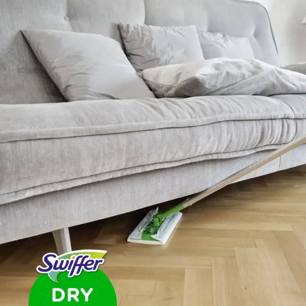 Swiffer anti-staub tücher trocken in grün und weiß auf holzboden unter grauem sofa liegend