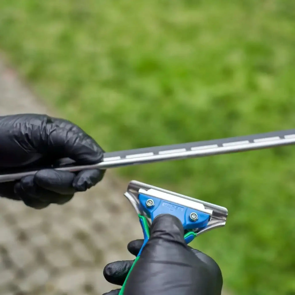 Unger green label fensterwischer mit blau-grünem griff und metallklinge gehalten von handschuhen vor gras