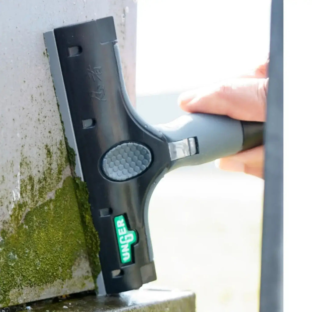 Black and gray unger Kunststoffklingen squeegee with textured grip handle used to remove green moss from surface