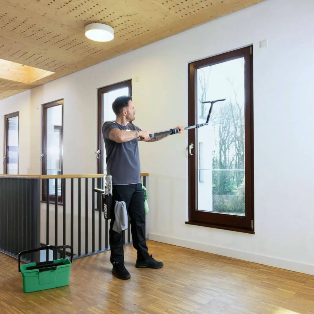 Ein mann verwendet das unger ninja 6in1 carbon-stangen-set akn19 mit langem griff und gummiwischer zum reinigen eines großen fensters