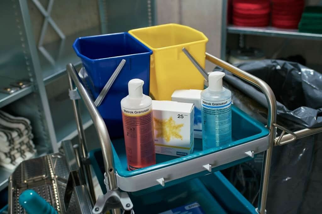 Blaue und gelbe plastik Eimer mit metallgriffen auf einem wagen neben flaschen wetrak granuusan desinfektionsmittel für wetrok granufloor bodenreiniger sticks