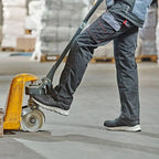 Schwarze arbeitshose mit mehreren taschen und roten nähte, getragen von einem arbeiter mit gelbem palettenhubwagen, kombiniert mit wica® lanzo 31540 halbschuhen s1p esd sra